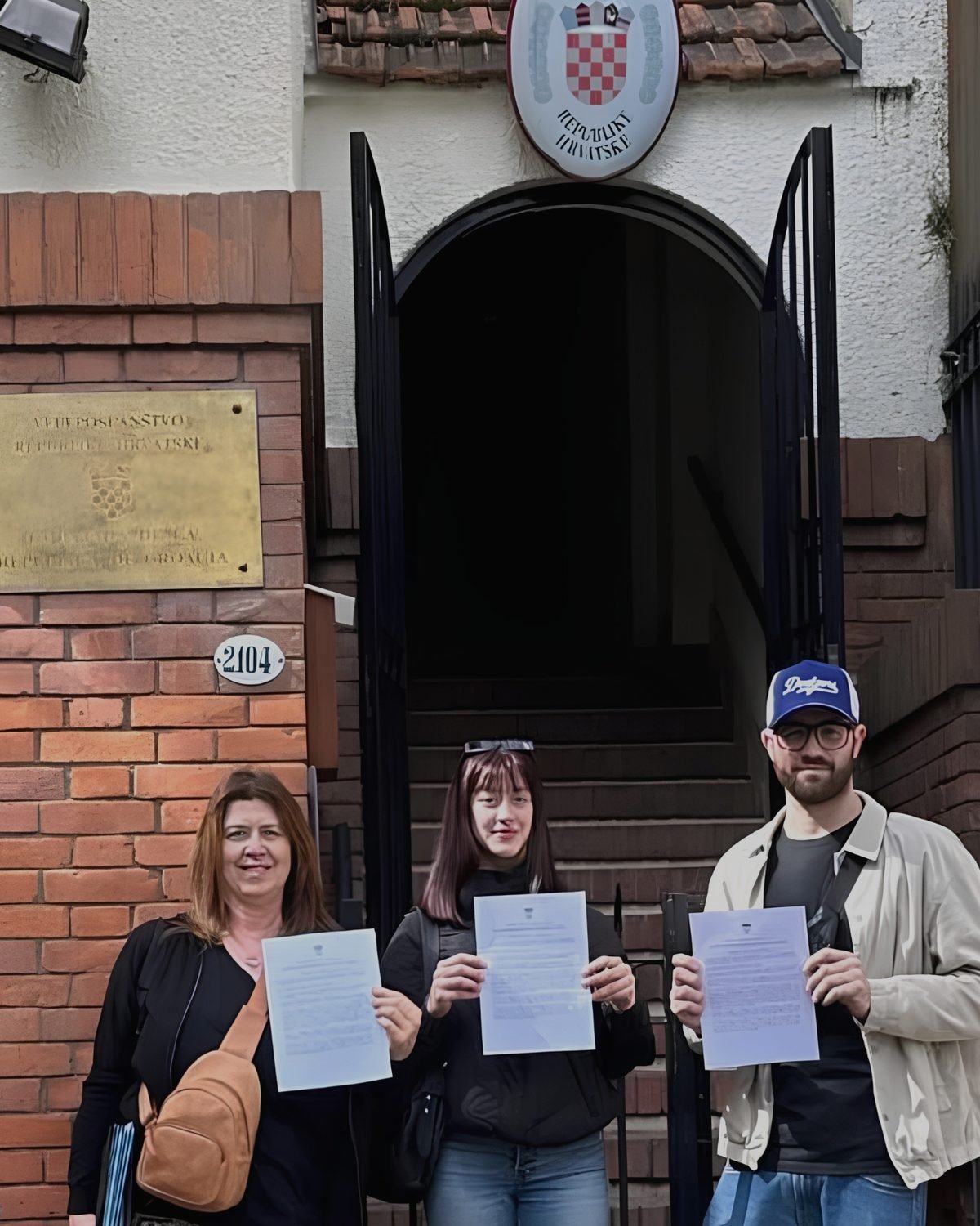 Tres personas sostienen su solicitud de ciudadanía croata en la puerta de la embajada