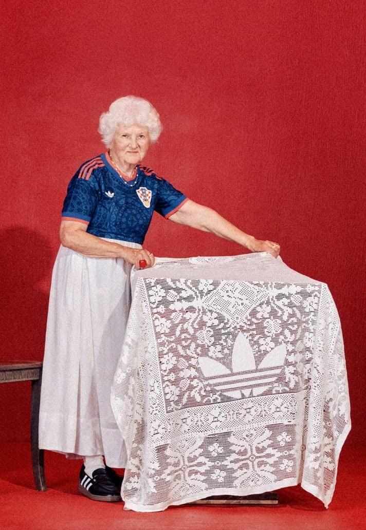 Una mujer mayor con la camiseta azul de Croacia y una falda blanca muestra un mantel de encaje sobre un fondo rojo
