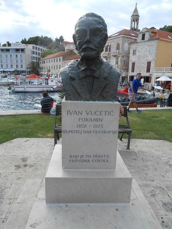 Busto de bronce de Ivan Vučetić sobre un pedestal de piedra con su nombre y una inscripción, frente al puerto de Hvar