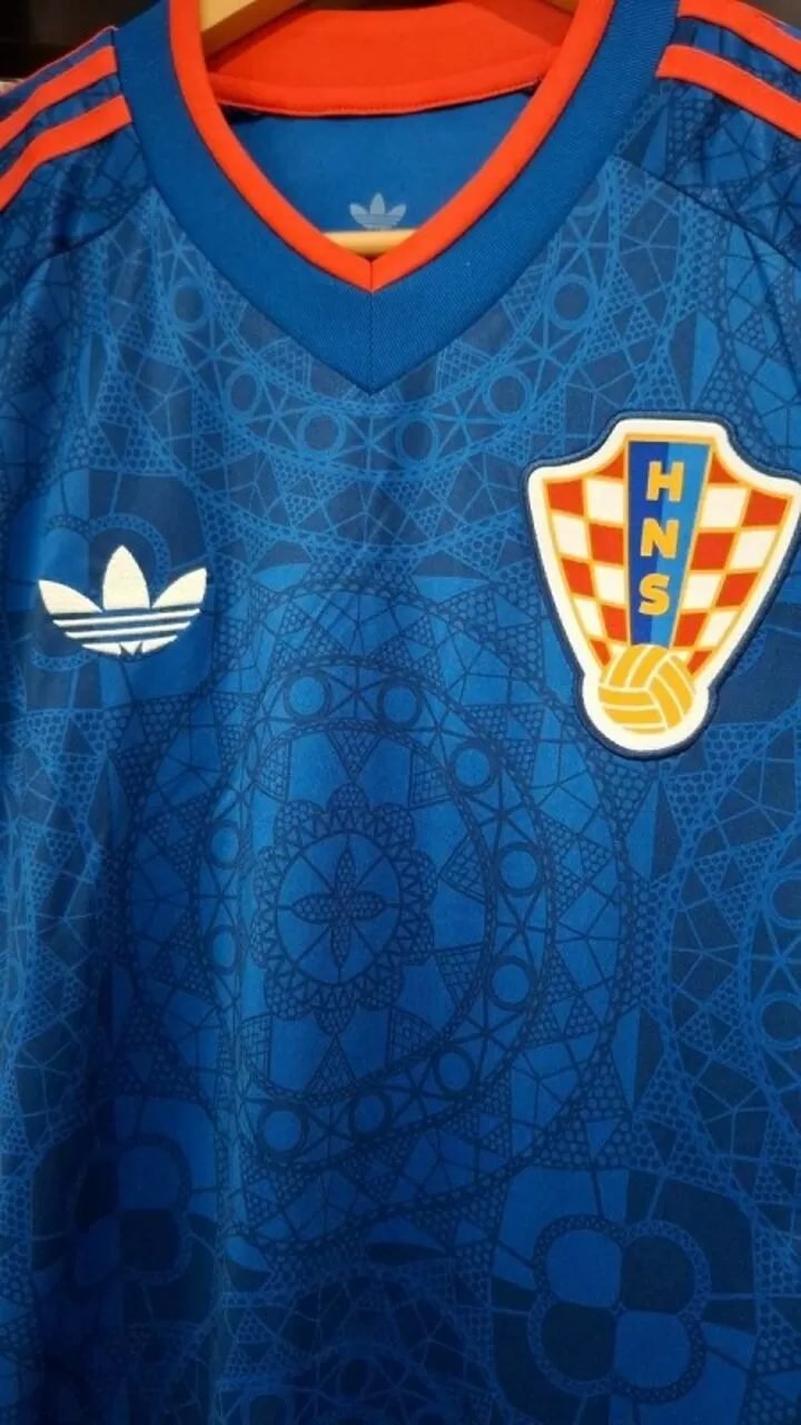 Primer plano de la camiseta azul con motivos de encaje, el escudo de la HNS y el trébol de adidas