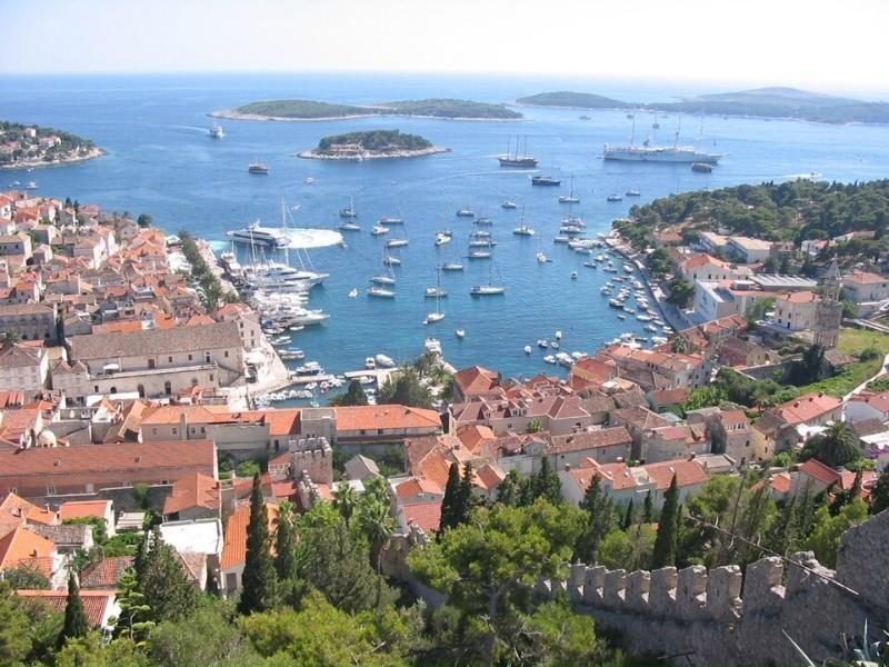 Vista aérea de la ciudad y el puerto de Hvar, con techos de tejas rojas, veleros y pequeñas islas en el Adriático