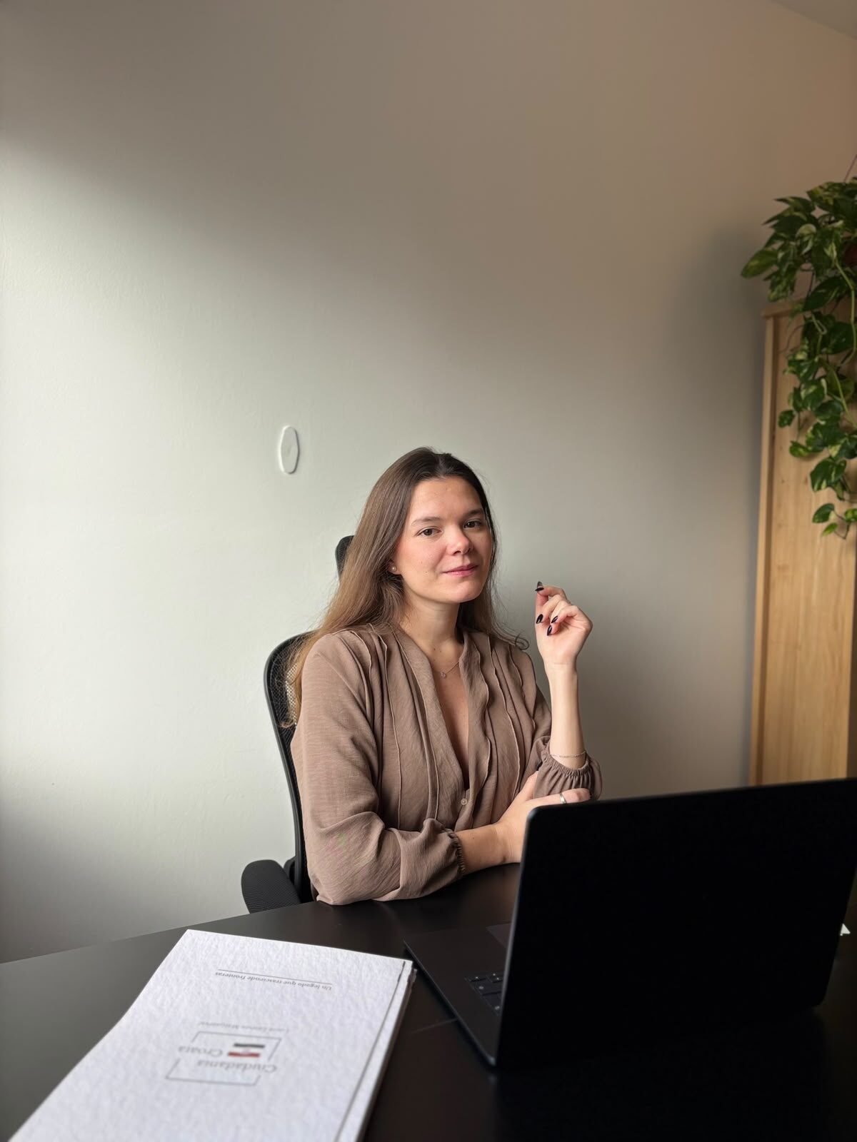 Lucía Lemos Matijašević sentada en su escritorio, con una blusa beige, junto a una laptop y la carpeta de Ciudadanía Croata