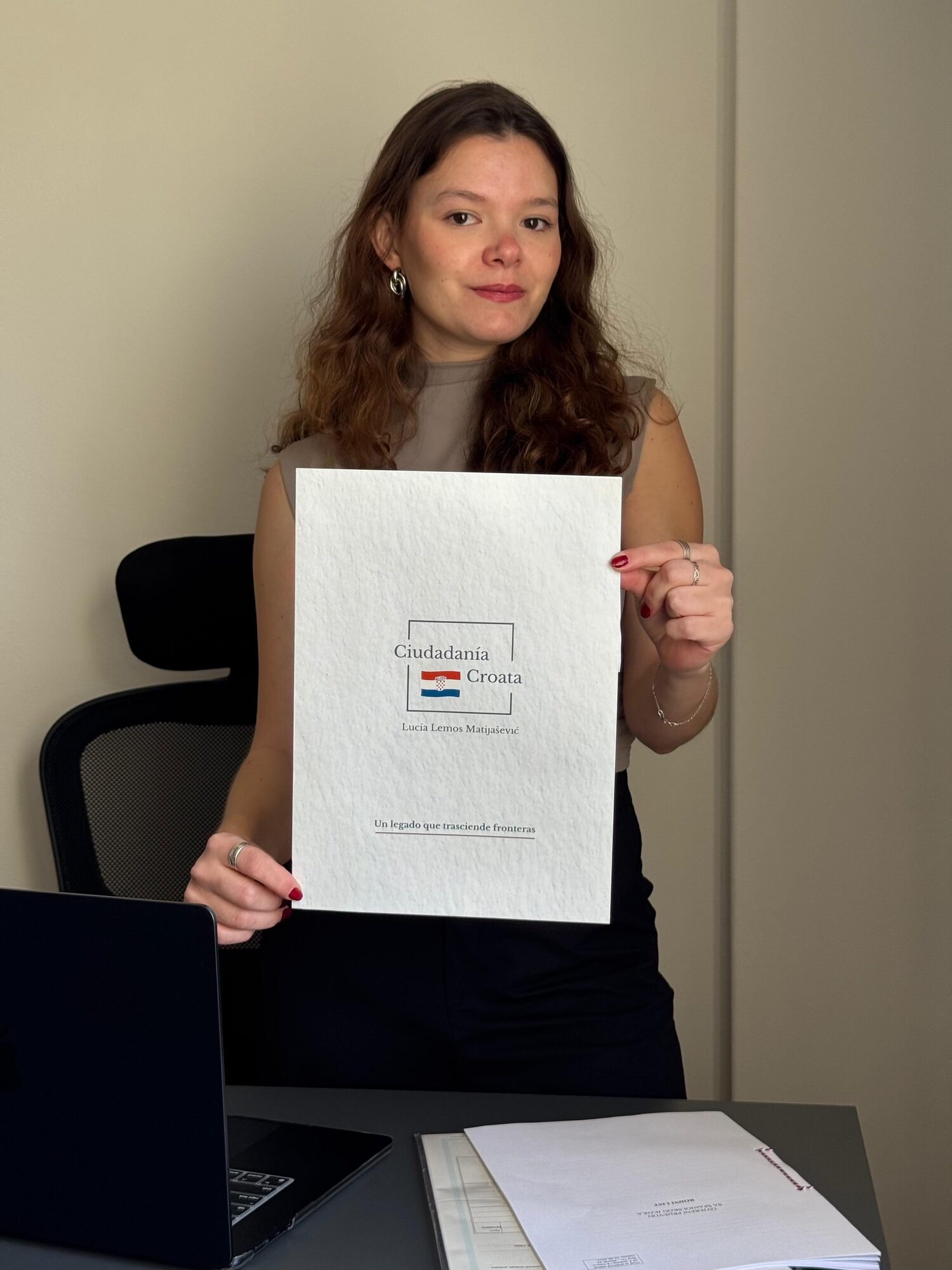 Lucía Lemos Matijašević de pie sostiene con las dos manos la carpeta blanca con el logo de Ciudadanía Croata