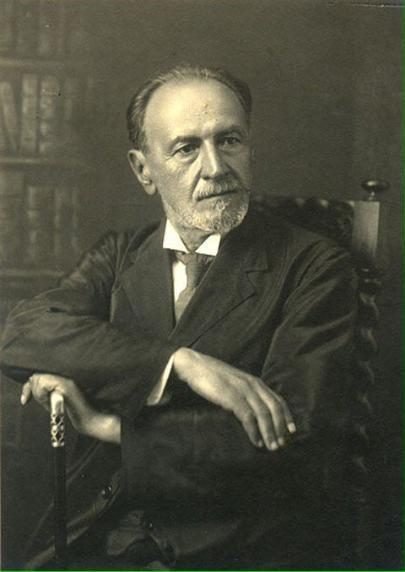 Retrato en blanco y negro de Juan Vucetich, un hombre mayor de barba canosa, sentado con las manos apoyadas sobre un bastón